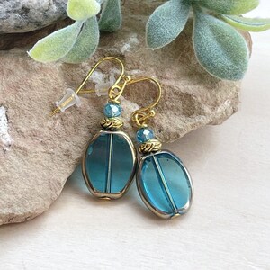 May include: A pair of gold tone earrings with teardrop shaped blue glass beads. The beads have a metallic finish and are accented with smaller gold beads.
