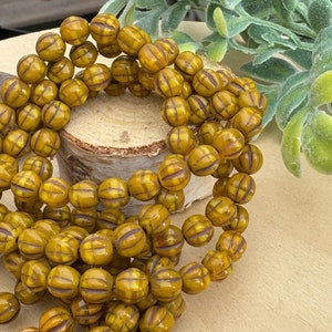 May include: A strand of yellow and brown striped glass beads. The beads are round and have a textured surface.