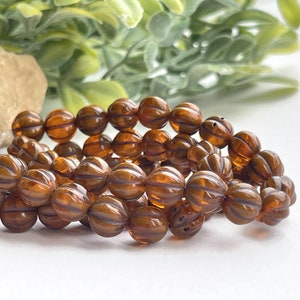 May include: A strand of brown glass beads with a ribbed texture. The beads are round and have a translucent appearance.