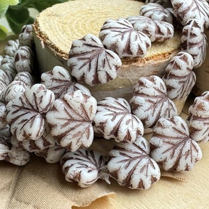 May include: A strand of white glass beads with a leaf design. The beads have a brown glaze and are strung together on a white cord.