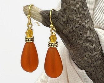 Könnte beinhalten: Ein Paar orangefarbene tropfenförmige Glasohrringe mit goldenen Akzenten und einem Perlmuster.