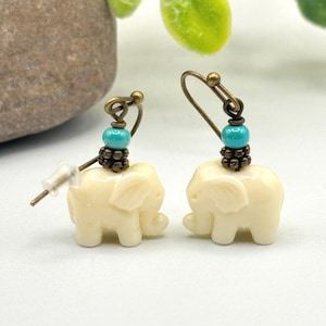 May include: A pair of dangle earrings featuring white elephant charms with turquoise beads and bronze accents.