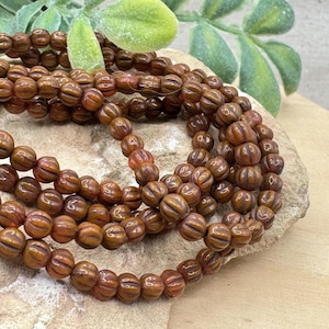 May include: A strand of brown glass beads with a ribbed texture. The beads are round and have a slightly translucent appearance.
