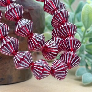 May include: A strand of red glass beads with white stripes. The beads are faceted and have a conical shape.