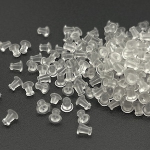 May include: A pile of clear, translucent earring backs. The earring backs are made of a soft, flexible material and are designed to secure earrings. The earring backs are small and have a mushroom-like shape.
