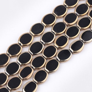 May include: A strand of black oval-shaped beads with gold trim. The beads are strung on a clear cord.