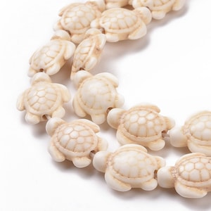 May include: A strand of white ceramic turtle beads. The beads are strung on a clear elastic cord and are all facing the same direction.