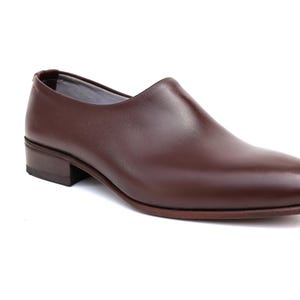 May include: A single brown leather shoe with a low heel. The shoe has a smooth, polished surface and a rounded toe. The shoe is a dark reddish-brown color and appears to be new. The shoe is designed for formal or business wear.