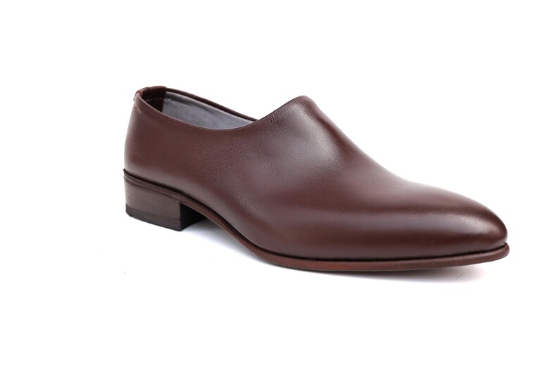 May include: A single brown leather shoe with a low heel. The shoe has a smooth, polished surface and a rounded toe. The shoe is a dark reddish-brown color and appears to be new. The shoe is designed for formal or business wear.