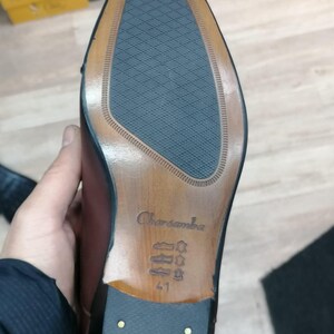 May include: Close-up of the sole of a brown leather dress shoe. The sole features a textured blue rubber insert, a wooden heel, and the brand name "Charsamba" is visible. Size 41 is stamped on the sole.