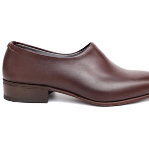 May include: A single brown leather shoe with a low heel. The shoe has a smooth, polished surface and a rounded toe. The design is minimalist and elegant, suitable for various occasions.