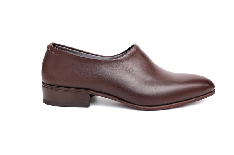 May include: A single brown leather shoe with a low heel. The shoe has a smooth, polished surface and a rounded toe. The design is minimalist and elegant, suitable for various occasions.