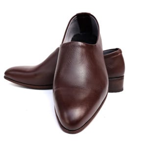 May include: A pair of brown leather shoes with a low heel. The shoes have a smooth, polished finish and a pointed toe. The shoes are set against a white background.