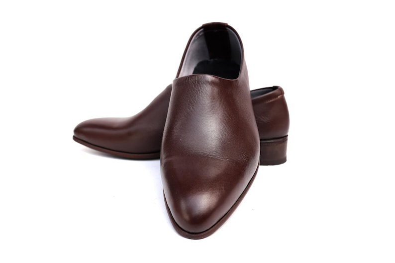 May include: A pair of brown leather shoes with a low heel. The shoes have a smooth, polished finish and a pointed toe. The shoes are set against a white background.