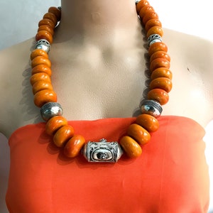 May include: A long necklace made of orange amber beads with silver accents. The necklace has a silver clasp in the center.