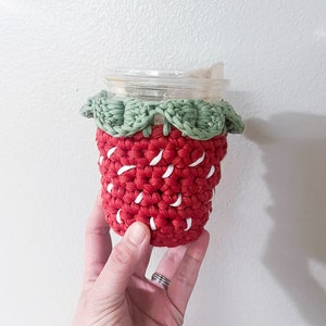 May include: Red and white crocheted strawberry-shaped cup cozy with green crocheted leaves.