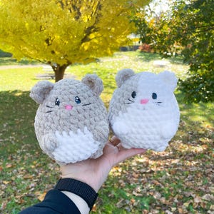 May include: Two crocheted plush toys shaped like mice. One is gray and white, the other is white. Both have pink embroidered noses and whiskers.