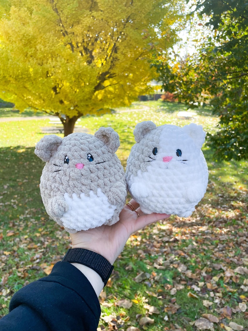 May include: Two crocheted plush toys shaped like mice. One is gray and white, the other is white. Both have pink embroidered noses and whiskers.