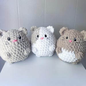 May include: Three crocheted hamster plushies. One is beige, one is white with beige accents, and one is beige with white accents.
