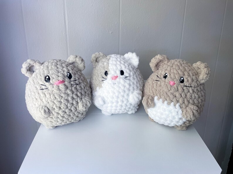 May include: Three crocheted hamster plushies. One is beige, one is white with beige accents, and one is beige with white accents.
