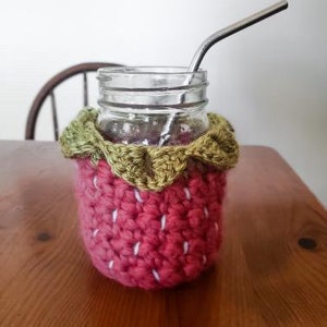 May include: A crocheted strawberry-shaped glass cozy with green leaves, a clear glass jar, and a metal drinking straw.