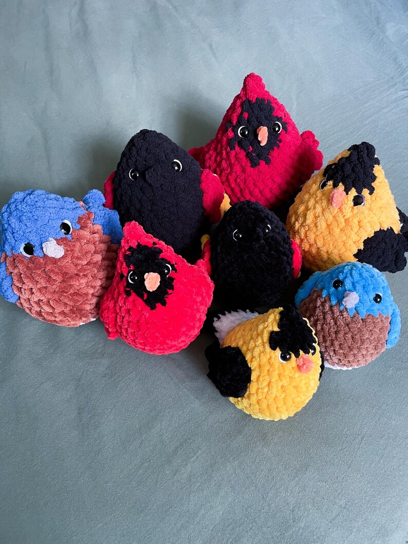 May include: A collection of eight crocheted bird plushies in various colors, including red, black, blue, yellow, and brown. The plushies have embroidered eyes and beaks.