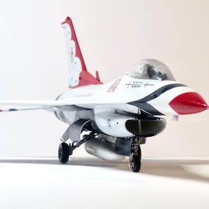 Puede incluir: Un avión modelo blanco y rojo con una franja negra y azul en el lateral. El avión tiene una cola roja con un diseño blanco y un cono de nariz negro.