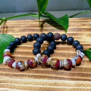 May include: Two bracelets, one black lava rock and one with brown, red, and white beads. The bracelets are stacked on top of each other.