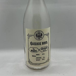 Puede incluir: Una botella de vidrio transparente con un tapón de corcho y una etiqueta que dice "КАЗЕННОЕ ВИНО." La etiqueta también incluye información sobre la fuerza del vino, su precio y su cantidad.