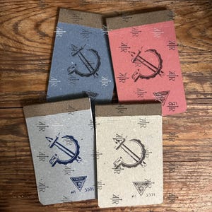 May include: Four small notepads in shades of blue, red, and tan, each with a brown binding. The notepads feature a hammer and sickle design and the text "CRETON" and "5571".
