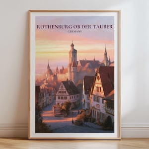 Op de afbeelding: Een ingelijste kunstprint met een schilderachtige illustratie van Rothenburg ob der Tauber, Duitsland. De afbeelding toont een stad met vakwerkhuizen en een kasteeltoren onder een zachte zonsonderganghemel. De tekst luidt ROTHENBURG OB DER TAUBER GERMANY.
