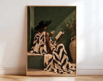 May include: A framed wall art print depicting a person wearing a wide-brimmed black hat and a flowing white garment with a black abstract pattern. The person holds a glass of white wine and an open book while sitting against a dark green wall.