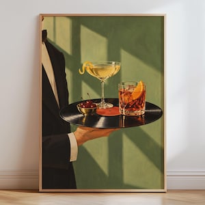 May include: A framed art print depicting a person in a black tuxedo jacket holding a black vinyl record as a serving tray. On the record sits a stemmed cocktail glass with a lemon twist, a rocks glass with an orange slice, and a small bowl of cherries.