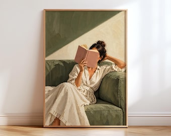 May include: A framed wall art print depicting a person with dark hair in a bun, wearing a cream-colored dress, sitting on a dark green sofa while holding an open pink book in front of their face. The background features a wall with diagonal light.