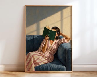 May include: A framed wall art print depicting a person sitting on a deep blue sofa, wearing a pink and white striped robe, and holding an open dark green book. The scene features soft sunlight casting shadows across a textured beige wall.
