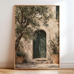 May include: A framed wall art print depicting a stone building facade with a dark green arched door. An olive tree with green leaves stands to the left, casting shadows on the light-coloured stone wall. Two terracotta pots with plants sit on the ground.