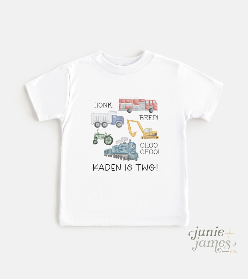 May include: White t-shirt featuring watercolor illustrations of various vehicles, including a fire truck, dump truck, tractor, excavator, and train. Text on the shirt reads "HONK!", "BEEP!", "CHOO CHOO!", and "KADEN IS TWO!"