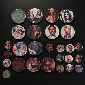 May include: A collection of circular pin-back buttons featuring various graphic designs, including portraits, movie-themed imagery, and text such as 'I Love Bush', 'Shane Heart Breaker', 'But I'm a Star', and 'Horror Whore', displayed alongside a US quarter.