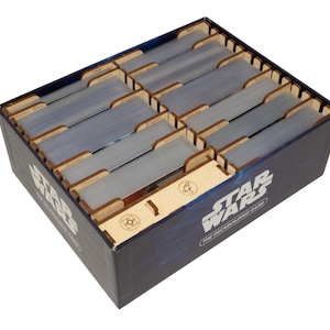 May include: A dark blue Star Wars The Deckbuilding Game box containing a light-coloured wooden card organiser insert. The insert features multiple slots filled with stacks of cards protected by clear plastic sleeves, with laser-cut dividers.