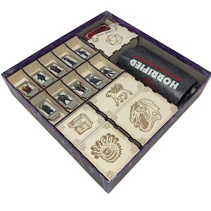May include: A wooden game organizer for the board game Horrified. The organizer has compartments for game pieces, cards, and dice. The box is purple with a wooden interior. The word "HORRIFIED" is printed on a black tube.