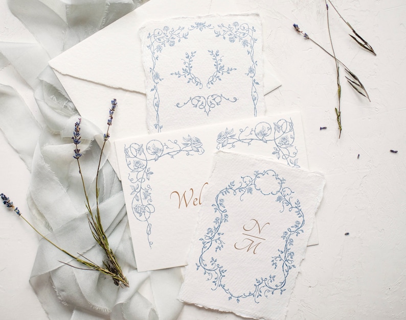 May include: Four white cards with blue floral designs. The cards have different designs, including a corner design, a full border design, and a monogram design. The monogram design includes the initials "N" and "M".