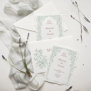 May include: Two wedding invitations with a green floral border and the text "With love, we invite you to celebrate the wedding of Martina & Daniel" printed in burgundy.