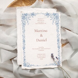 May include: Wedding invitation with a blue floral border. The invitation is for Martina & Daniel, hosted by the Haskell and Santiago families. The wedding will take place in Chileno Bay, Los Cabos, Mexico.