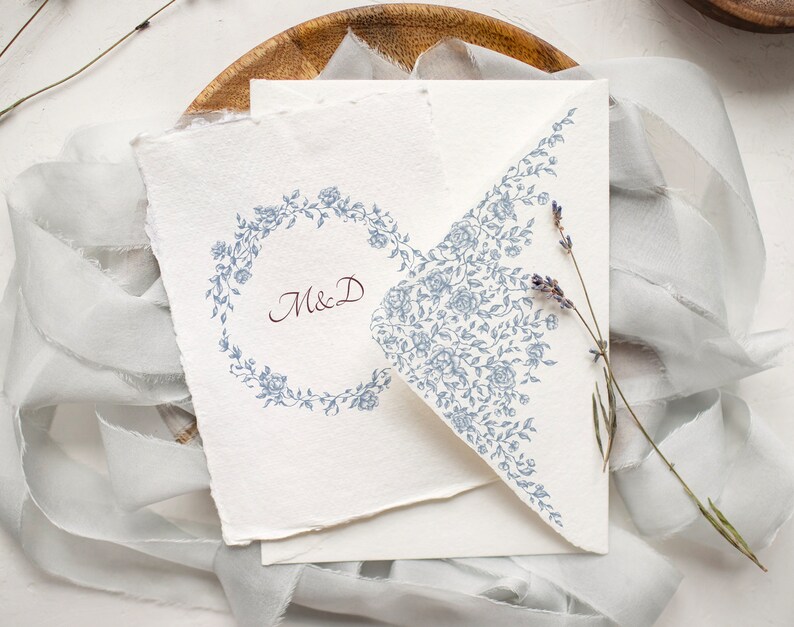 May include: A white card with a blue floral design on the envelope flap. The card has a blue floral wreath with the initials "M&D" in the center.