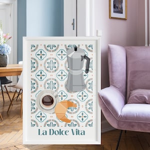 Puede incluir: Impresión artística enmarcada con una cafetera, una taza de café y un diseño de croissant sobre un fondo estampado. Las palabras "La Dolce Vita" están en la parte inferior. La impresión se muestra en una habitación con un sillón rosa y pisos de madera.