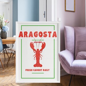 Op de afbeelding: Een ingelijste poster met een witte achtergrond toont het woord "ARAGOSTA" in rood, boven een rode kreeftenillustratie. Het woord "SEAFOOD" staat eronder en "FRESH CAUGHT DAILY" staat onderaan. De poster zit in een witte lijst.