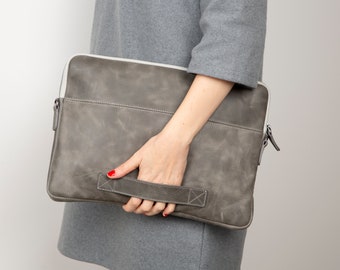May include: A gray leather laptop sleeve with a white zipper and a gray leather handle.