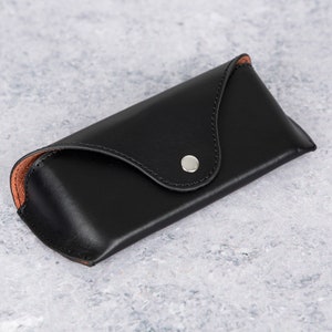 May include: A black leather glasses case with a brown leather lining and a silver snap closure.
