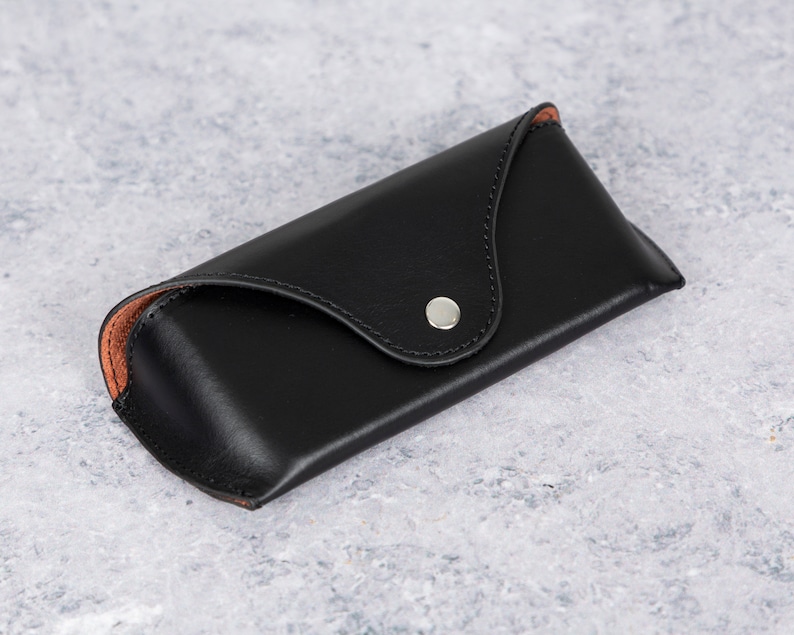 May include: A black leather glasses case with a brown leather lining and a silver snap closure.