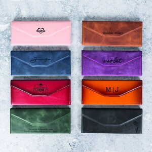 Pode incluir: Uma cole&ccedil;&atilde;o de oito estojos de &oacute;culos de couro em v&aacute;rias cores, incluindo rosa, azul, vermelho, castanho, roxo, laranja, verde e preto. Cada estojo apresenta um design ou inscri&ccedil;&atilde;o &uacute;nica, como nomes, iniciais ou cita&ccedil;&otilde;es. Os estojos s&atilde;o retangulares com fecho de aba.